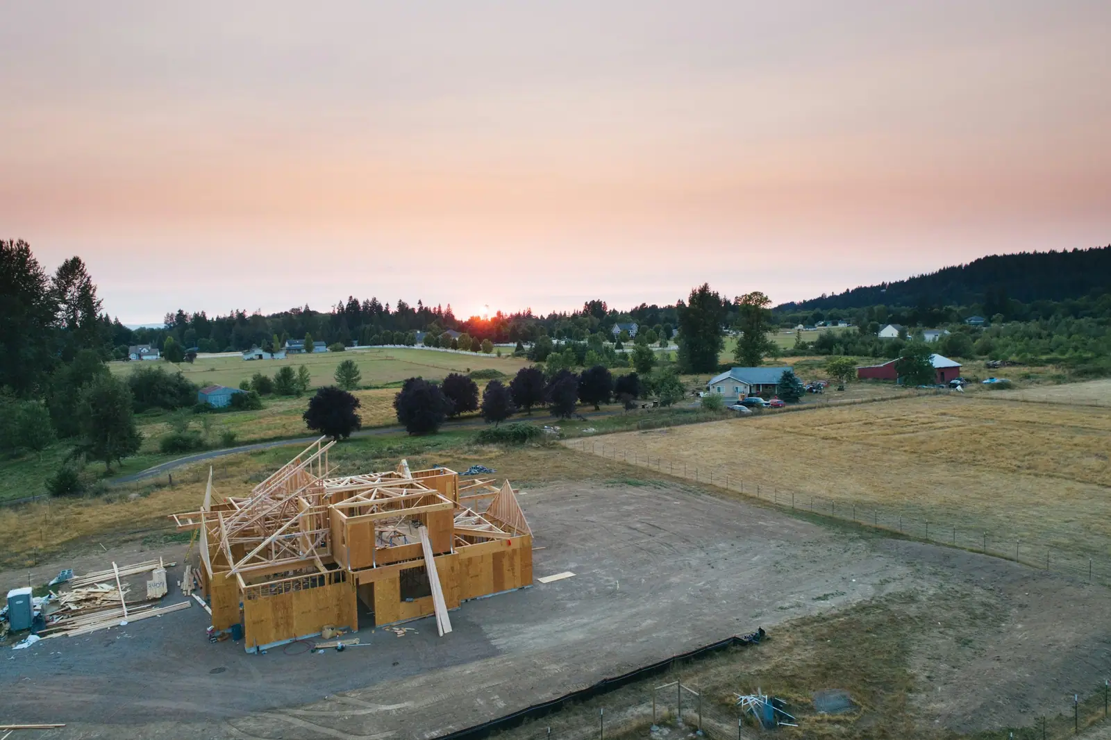 Timber frame of a new house on an open lot with hills and evening sky behind