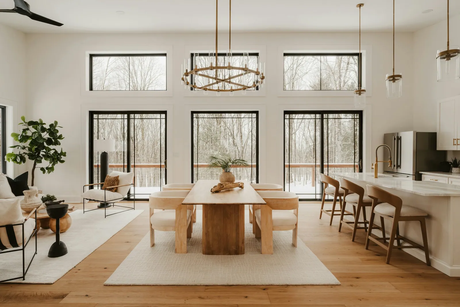 Bright great room with a long dining table, tall black-framed windows and oak floors
