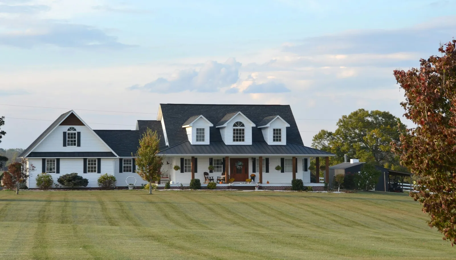 Large white country house with dormers and a deep front porch on a wide lawn