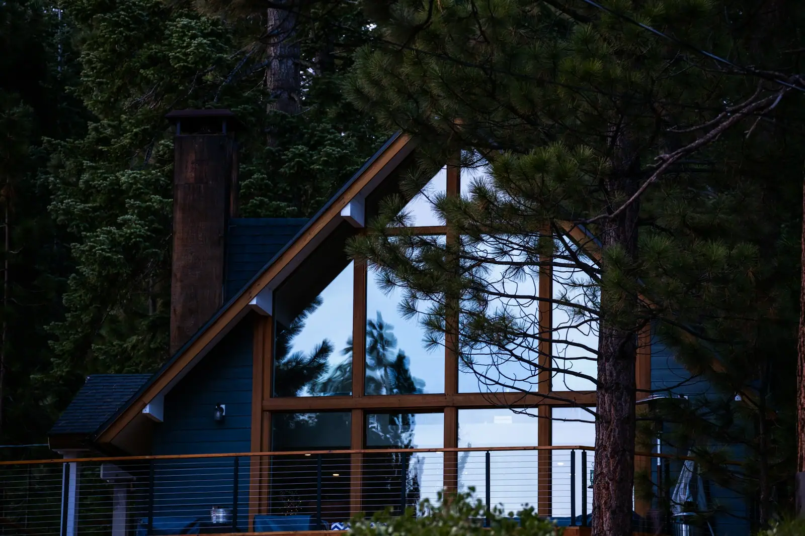 Cedar house with a tall glass gable lit from inside at dusk, set among pines